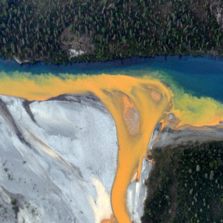Una vista aérea del río Kutuk en el Parque Nacional Puertas del Ártico de Alaska que parece pintura naranja derramándose en el agua azul clara.