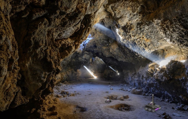 En esta imagen artística del escenario de las migas de pan, se pueden ver vehículos autónomos explorando un tubo de lava tras ser desplegados por un vehículo madre que permanece en la entrada para mantener el contacto con un orbitador o un dirigible.