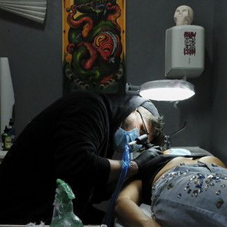 Archivo - Un tatuador de Negro Marfil Tattoo (C/ Elfo, 70) realiza un tatuaje a una clienta. Este estudio lleva desde el día 4 de mayo abierto, cuando se reabrieron pequeños comercios para atender a