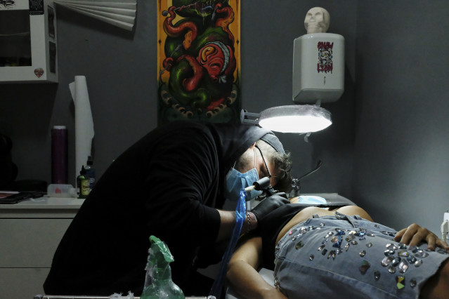 Archivo - Un tatuador de Negro Marfil Tattoo (C/ Elfo, 70) realiza un tatuaje a una clienta. Este estudio lleva desde el día 4 de mayo abierto, cuando se reabrieron pequeños comercios para atender a clientes, atendiendo con cita previa y de uno en uno sie