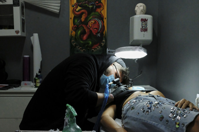 Archivo - Un tatuador de Negro Marfil Tattoo (C/ Elfo, 70) realiza un tatuaje a una clienta. Este estudio lleva desde el día 4 de mayo abierto, cuando se reabrieron pequeños comercios para atender a