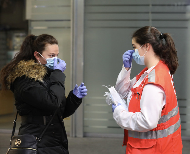 Archivo - Una voluntaria de Cruz Roja da indicaciones a una pasajera sobre cómo ponerse una mascarilla en la estación de Cercanías de Atocha durante el segundo día de reparto de mascarillas en el transporte público por la reactivación de la actividad labo
