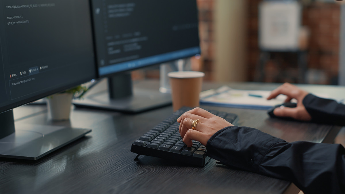 Closeup developer hands typing code keyboard while looking computer screens with programming interface software programmer sitting desk with clipboard writing algorithm