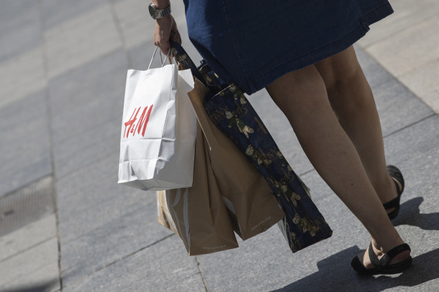 Archivo - Una mujer pasea cargada con varias bolsas, una de ellas perteneciente a la tienda H&M a 26 de junio de 2020.