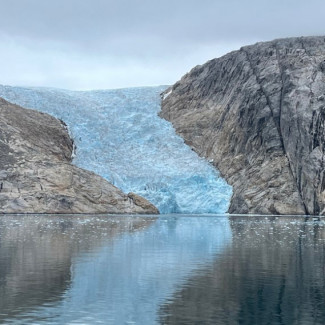 Entre dos colinas rocosas, un glaciar azul helado fluye hacia abajo y se encuentra con el agua.