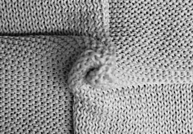 Un primer plano de un tejido de punto autoplegable, que demuestra cómo patrones de puntadas específicos (puntos derechos y reveses) codifican reglas geométricas que dictan la forma tridimensional del material.