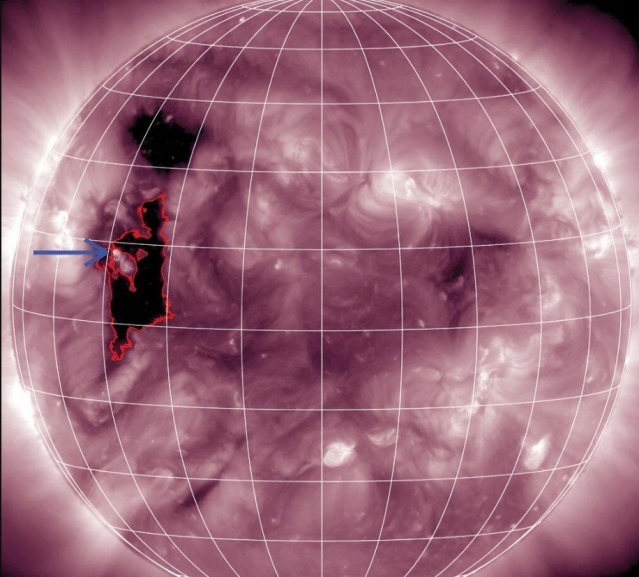 La flecha azul marca un pequeño punto brillante ubicado en el borde de un agujero coronal (delineado en rojo) que fue la fuente del fenómeno.