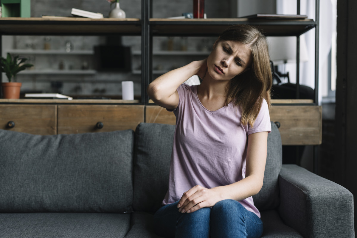 Mujer sentada en el sofa sufriendo de dolor de cuello