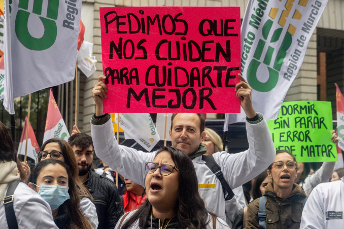 Manifestante con pancarta con lema 'Pedimos que nos cuiden para cuidarte mejor' durante la manifestación ‘Todos unidos por un objetivo común: el estatuto propio’, a 15 de noviembre de 2025, en M