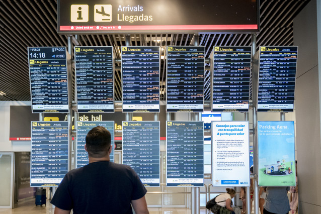 Archivo - Un turista observa el panel de llegadas en el aeropuerto.
