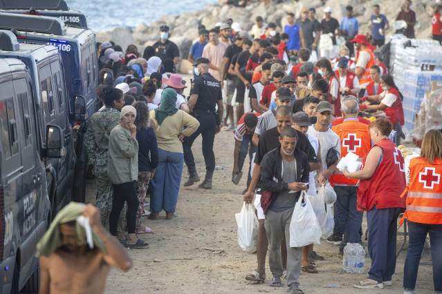 Miembros de la Cruz Roja atienden a varios inmigrantes, en la playa del Trampolín, a 20 de agosto de 2026, en Ceuta (España). El Ministerio de Defensa ha aprobado que más de un centenar de militares procedentes de Canarias se desplacen a Ceuta para reforz