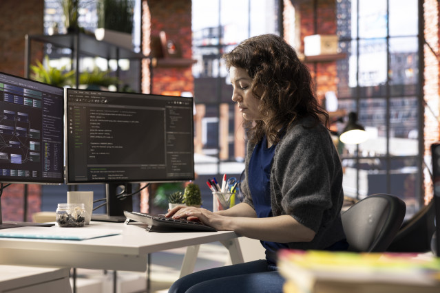 Archivo - Software engineer works on dual monitors and typing code for a development project. Technical developer multitasking, debugging and using advanced digital tools for coding.